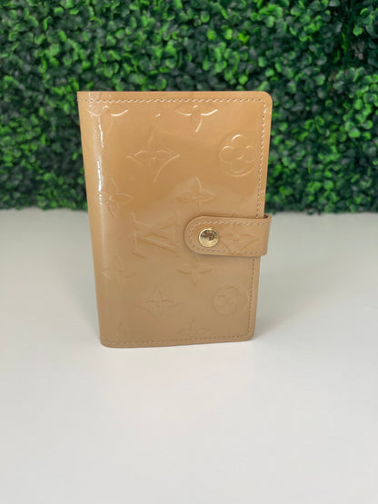 Front view of a preowned Louis Vuitton tan vernis leather wallet with a monogram pattern and a tan leather interior, featuring a lock and key mechanism.