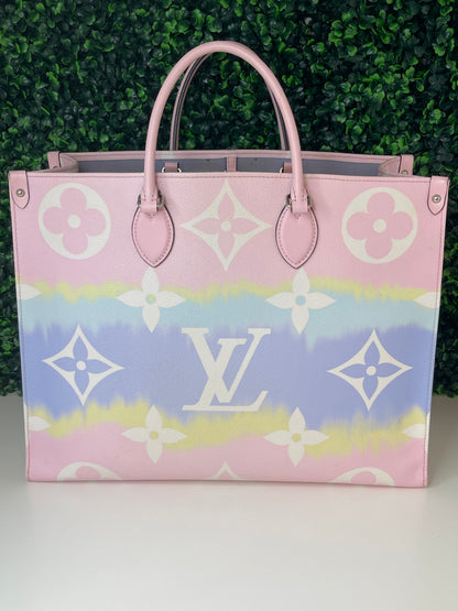 A pink and multicolor patterned Louis Vuitton OnTheGo Escale handbag GM with a structured handle and straps, displayed against a green leafy backdrop.