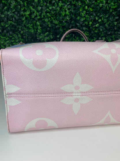 Zoomed in image of bottom corner view of a pink base and multicolor patterned Louis Vuitton OnTheGo Escale handbag GM laying on its side.