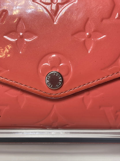 Zoomed in image of front view of a pink glossy preowned Louis Vuitton long wallet with vernis leather and a front flap snap, silver hardware button snap.