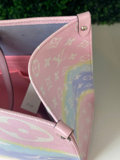 Zoomed in image of top corner view of a pink base and multicolor patterned Louis Vuitton OnTheGo Escale handbag GM looking inside.