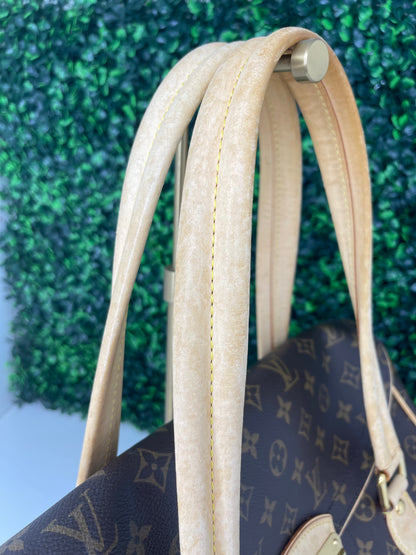 Zoomed in photo of tan leather handle straps on a preowned Louis Vuitton Monogram Beverly GM handbag with a brown and beige color scheme, featuring the brand's iconic LV logo, tan leather trim, displayed against a green-tone background.