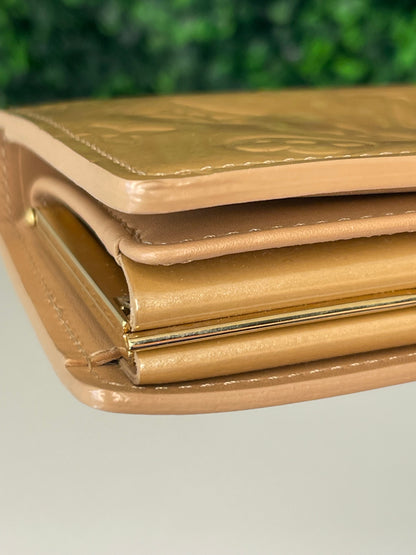 Bottom corner of a preowned Louis Vuitton tan vernis leather wallet with a monogram pattern and a tan leather interior.