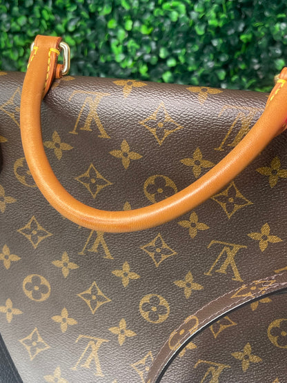 Backside view of a preowned Louis Vuitton Marignan handbag in black color with a brown leather handle. 