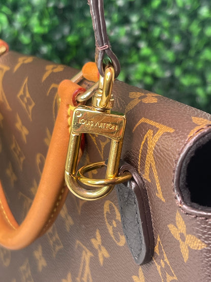 Metal clasp of gold hardware of a preowned Louis Vuitton Marignan handbag in black color with a brown handle and a gold-tone hardware.