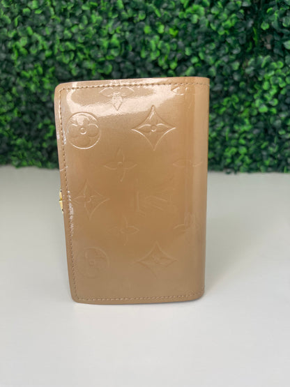 Back view of a preowned Louis Vuitton tan vernis leather wallet with a monogram pattern and a tan leather interior, featuring a lock and key mechanism.