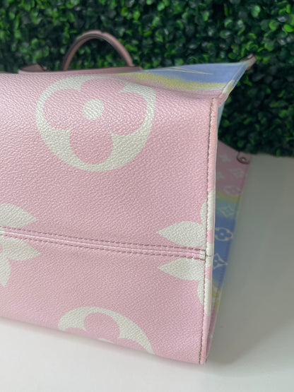 Zoomed in image of bottom corner view of a pink base and multicolor patterned Louis Vuitton OnTheGo Escale handbag GM laying on its side.