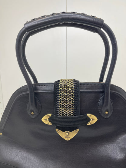 Front view of a preowned Dior black leather handbag with black suede trim and aged brass hardware, featuring a braided top handle.