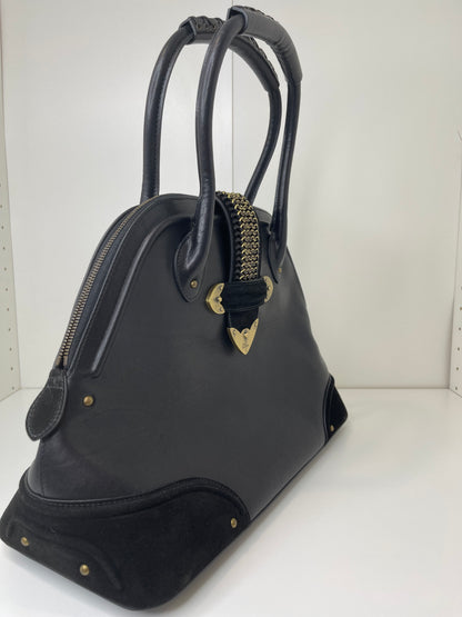 Side view of a preowned Dior black leather handbag with black suede trim and aged brass hardware, featuring a braided top handle.