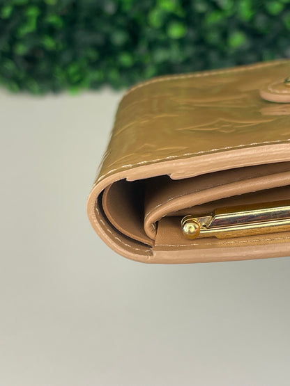 Bottom corner of a preowned Louis Vuitton tan vernis leather wallet with a monogram pattern and a tan leather interior.