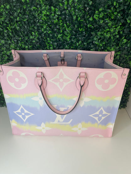 A pink and multicolor patterned Louis Vuitton OnTheGo Escale handbag GM with a structured handle and straps, displayed against a green leafy backdrop.