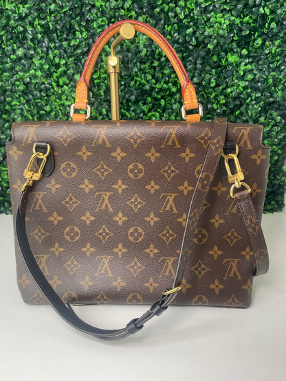 A preowned Louis Vuitton Marignan handbag in black color with a brown handle and a gold-tone hardware. View from the backside of handbag. Showing metal clasp on backside. 