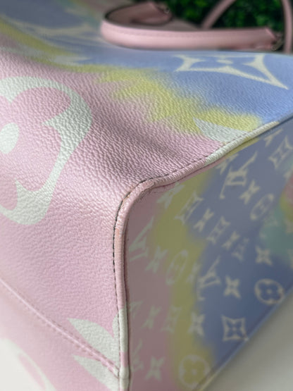 Zoomed in image of bottom corner view of a pink base and multicolor patterned Louis Vuitton OnTheGo Escale handbag GM laying on its side. Image shows minor rubs to corner.