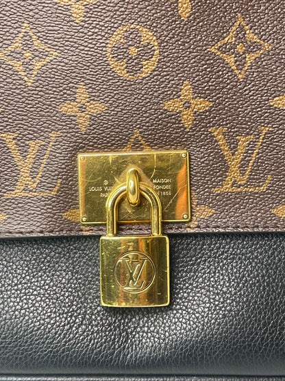 A preowned Louis Vuitton Marignan handbag in black color with a brown handle and a gold-tone hardware. Image shows zoomed in gold hardware with label. 