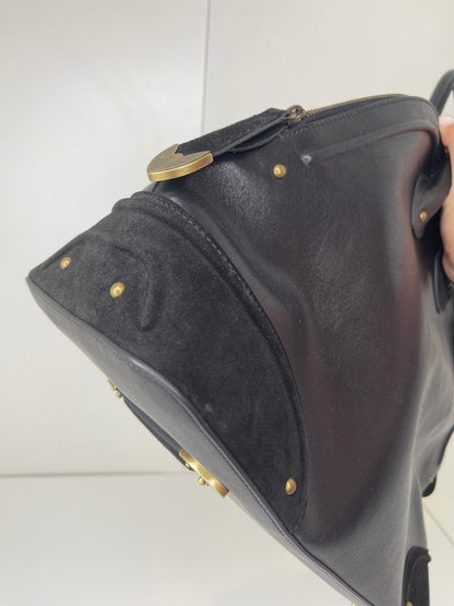 Bottom corner view of a preowned Dior black leather handbag with black suede trim and aged brass hardware.