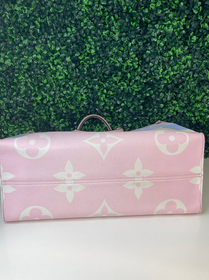 Bottom view of a pink base and multicolor patterned Louis Vuitton OnTheGo Escale handbag GM laying on its side.