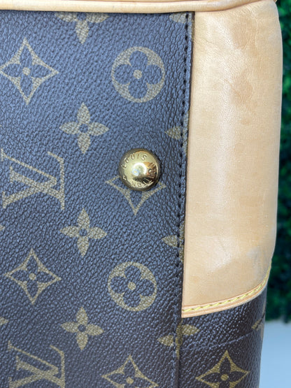 Bottom corner of a preowned Louis Vuitton Monogram Beverly GM handbag with a brown and beige color scheme, tan leather trim, featuring the brand's iconic LV logo and gold hardware.
