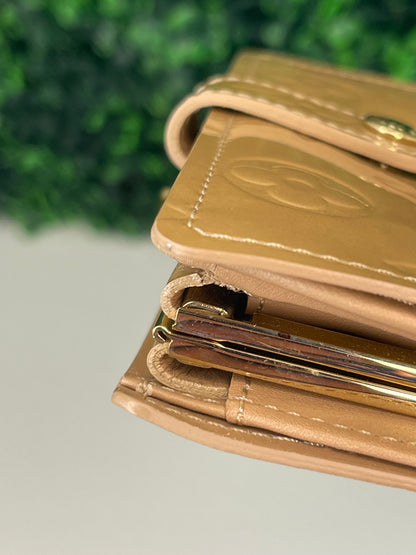Corner of a preowned Louis Vuitton tan vernis leather wallet with a monogram pattern and a tan leather interior, featuring a lock and key mechanism.