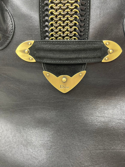 Zoomed image of the front suede clasp and Dior logo on a preowned Dior black leather handbag with black suede trim and aged brass hardware.