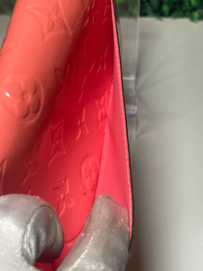 Interior slip pocket on backside of a pink glossy preowned Louis Vuitton long wallet with vernis leather.