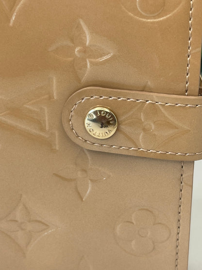 Gold button clasp hardware on a preowned Louis Vuitton tan vernis leather wallet with a monogram pattern.